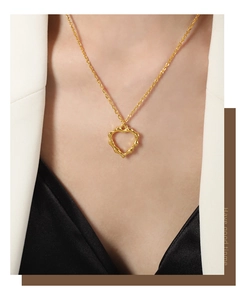 Detailweergave van een gouden hartvormige hanger ketting met golvende textuur bij een model