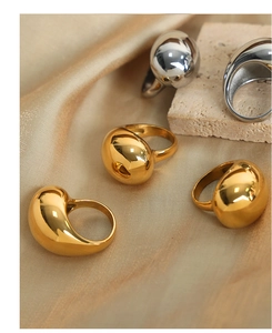 Detailed close-up of chunky gold and silver teardrop rings on luxury silk and stone texture