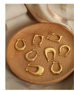 Vista detallada de varios pendientes geométricos bañados en oro sobre bandeja de madera