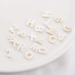 Handmade white freshwater shell letter beads in a white ceramic dish for DIY jewelry