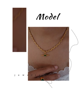 Detail of gold wave chain necklace with rectangular green stone pendant on model