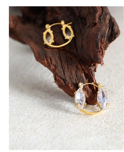 Macro shot of gold hoop earrings with marquise-cut zircons on a textured surface