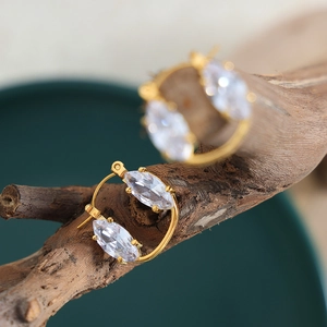 Gold hoop earrings with marquise-cut white crystals on a rustic wooden branch