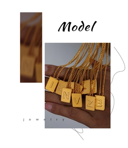 Macro detail of gold square letter pendant necklaces with embossed engraving and thin chains