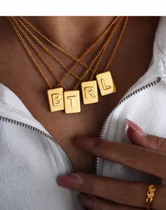 Close-up of model wearing layered gold square letter pendant necklaces in stainless steel