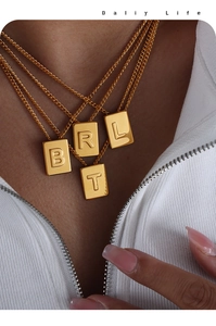 Close-up of gold-plated square initial pendant necklaces layered on a female model