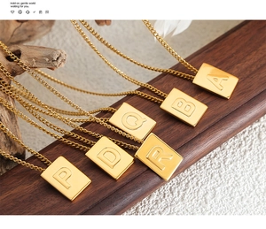 Detail of gold square pendant necklaces featuring embossed alphabet letters A-Z