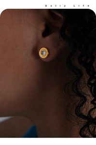 Gros plan d'un modèle portant un clou d'oreille rond doré serti d'un zircon brillant