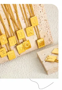 Detail of golden square letter pendants on travertine stand with minimalist crossbody chains