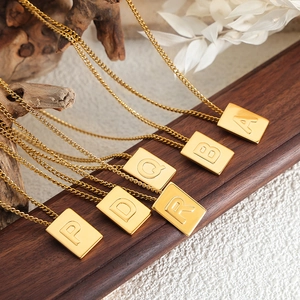 Golden titanium steel square alphabet pendant necklace on rustic wooden display stand