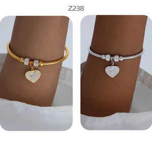 Dettaglio dei bracciali a serpente color oro e argento con ciondoli a cuore e strass