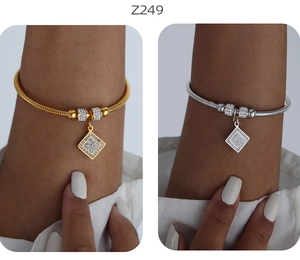 Dettaglio di bracciali in oro e argento con ciondoli geometrici e zirconi scintillanti