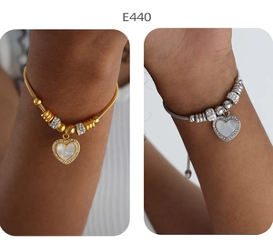 Detail eines Herzanhänger-Armbands in Gold und Silber mit schimmernder Perlmutt-Einlage