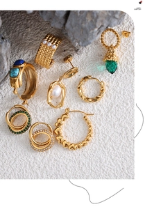 Détails de boucles d'oreilles et bagues en titane doré disposées sur des pierres naturelles