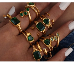 Dettaglio di anelli d'oro impilati con pietre verde smeraldo su sfondo denim