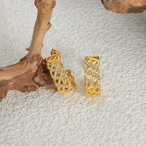Golden C-shaped woven geometric earrings with crystal accents on a natural wood base