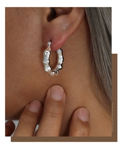 Detalle macro de pendientes de aro plateados con textura de bambú usados por una modelo