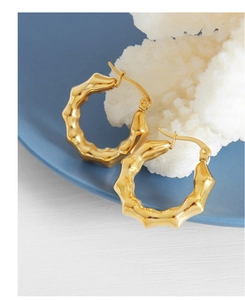 Primer plano de pendientes en C de oro de 18k con textura de ondas sobre coral blanco