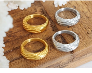 Dettaglio di anelli color oro e argento con trama a spirale su sfondo in legno