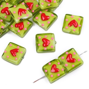 Macro shot of green glass heart square beads with pink polka dots for DIY jewelry