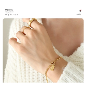 Detail van gouden armband met munt hanger en parelring op een witte gebreide trui