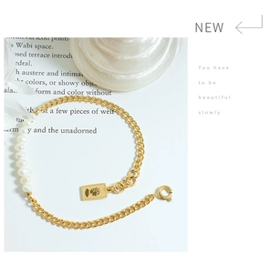 Detailopname van gouden armband met zoetwaterparels en een koningin munt hanger in vintage stijl