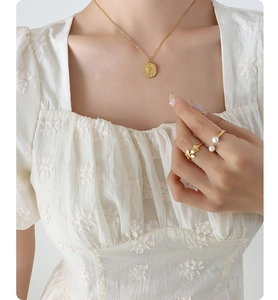 Nahaufnahme der goldenen Rosen-Halskette und Vintage-Ringe an Modell mit weißer Bluse