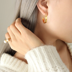 Orecchini a cerchio dorati minimalisti e anello di perle con un maglione bianco in maglia