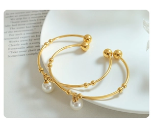 Detailed view of two gold titanium bracelets with white imitation pearl pendants on ceramic