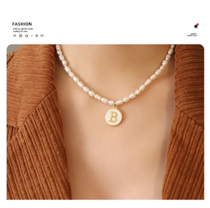Detail of baroque pearl necklace with a vintage gold letter B pendant on a model