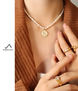 Detail of freshwater pearl necklace with gold letter E pendant on mother of pearl base