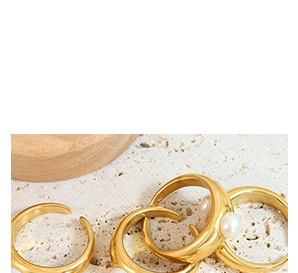 Detailed close-up of adjustable gold open rings with pearls on natural travertine stone