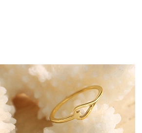 Close-up of golden geometric hollow heart ring on a white coral textured display