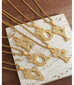 Close-up of gold crown initial pendants with zircons on a white textured stone base
