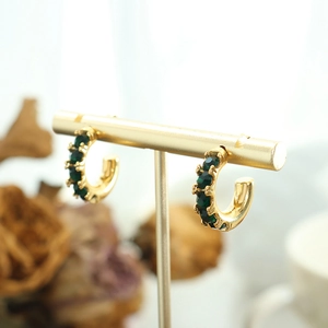 Boucles d'oreilles créoles dorées en C avec zircons verts sur support à bijoux doré