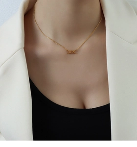 Dettaglio di una collana dorata con pendente a farfalla XO indossata con un blazer