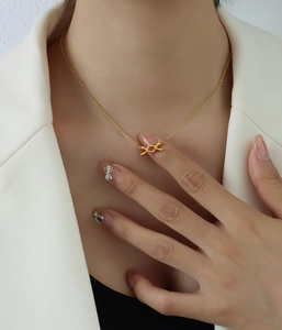 Elegante collana con ciondolo a fiocco dorato su modella con blazer bianco chic