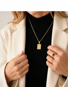 Dettaglio di una collana dorata con pendente lettera F e anelli d'oro indossati da una modella