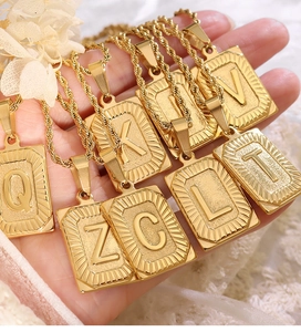 Dettaglio della collana con pendente quadrato dorato con lettera goffrata e texture