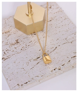 Close-up of minimalist golden padlock pendant necklace on a textured stone display