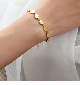 Detail of a gold-plated smiley face chain bracelet on a wrist with adjustable closure