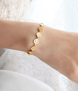 Detail showing golden smiley face charm bracelet on wrist with white fabric background