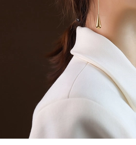 Close-up of golden teardrop earring with polished finish on model with white blazer