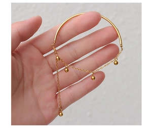 Detail of gold titanium steel bangle with half chain design and round bead tassel charms