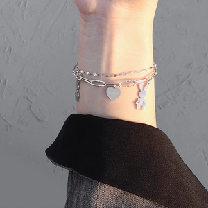 Double-layered silver bracelet with bunny and heart charms worn on a female wrist