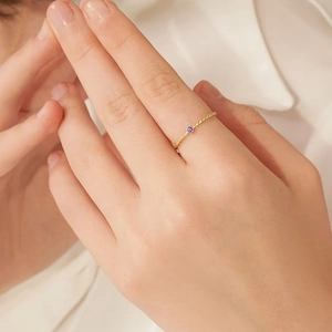 Twisted 18K gold plated stainless steel ring featuring a round purple zircon on model hand