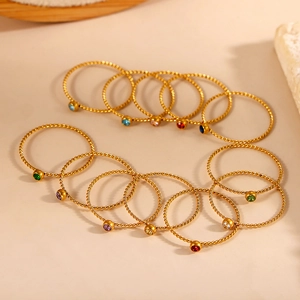 Detailed set of 12 twisted gold rings with vibrant birthstones on warm background