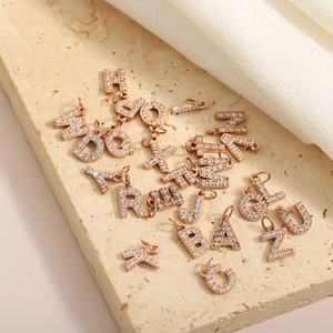 Macro view of rose gold micro-paved zircon alphabet pendants on stone and fabric background