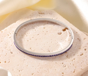 Detailaufnahme des silbernen Edelstahlarmbands mit lila Kristallen auf Steinuntergrund