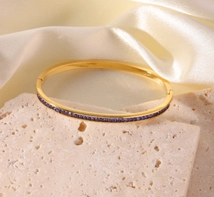 Makroaufnahme eines goldenen Edelstahl-Armreifs mit lila Kristallen auf weißer Seide
